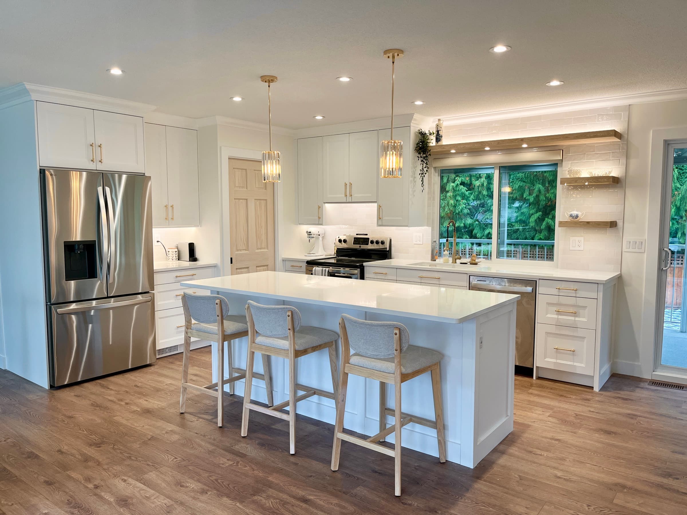 Renovated galley kitchen with white shaker cabinets, brass pulls, quartz island and three woven counter stools